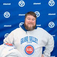 Gentleman with GV/Pistons crewneck on in front of GV Alumni backdrop, holding two other crewnecks